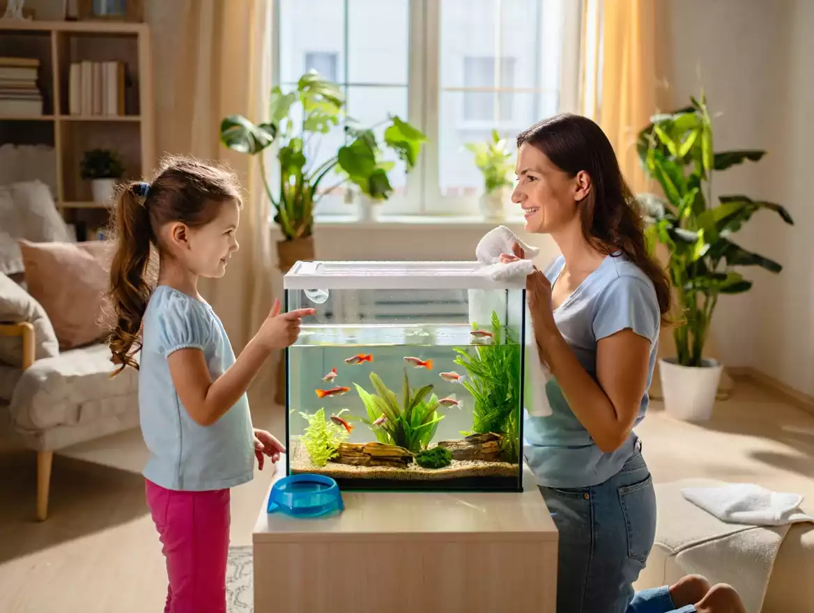Maman et sa fille nettoyant ensemble un aquarium d’eau douce dans un salon lumineux et chaleureux.